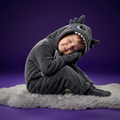 Child wearing a shark onesie sitting on a fluffy rug with a purple background